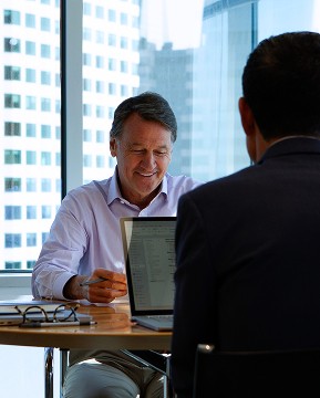 Contact Us. Let’s connect. CEO Will Muggia in a meeting with windows in the background that display the Boston Financial District skyline.