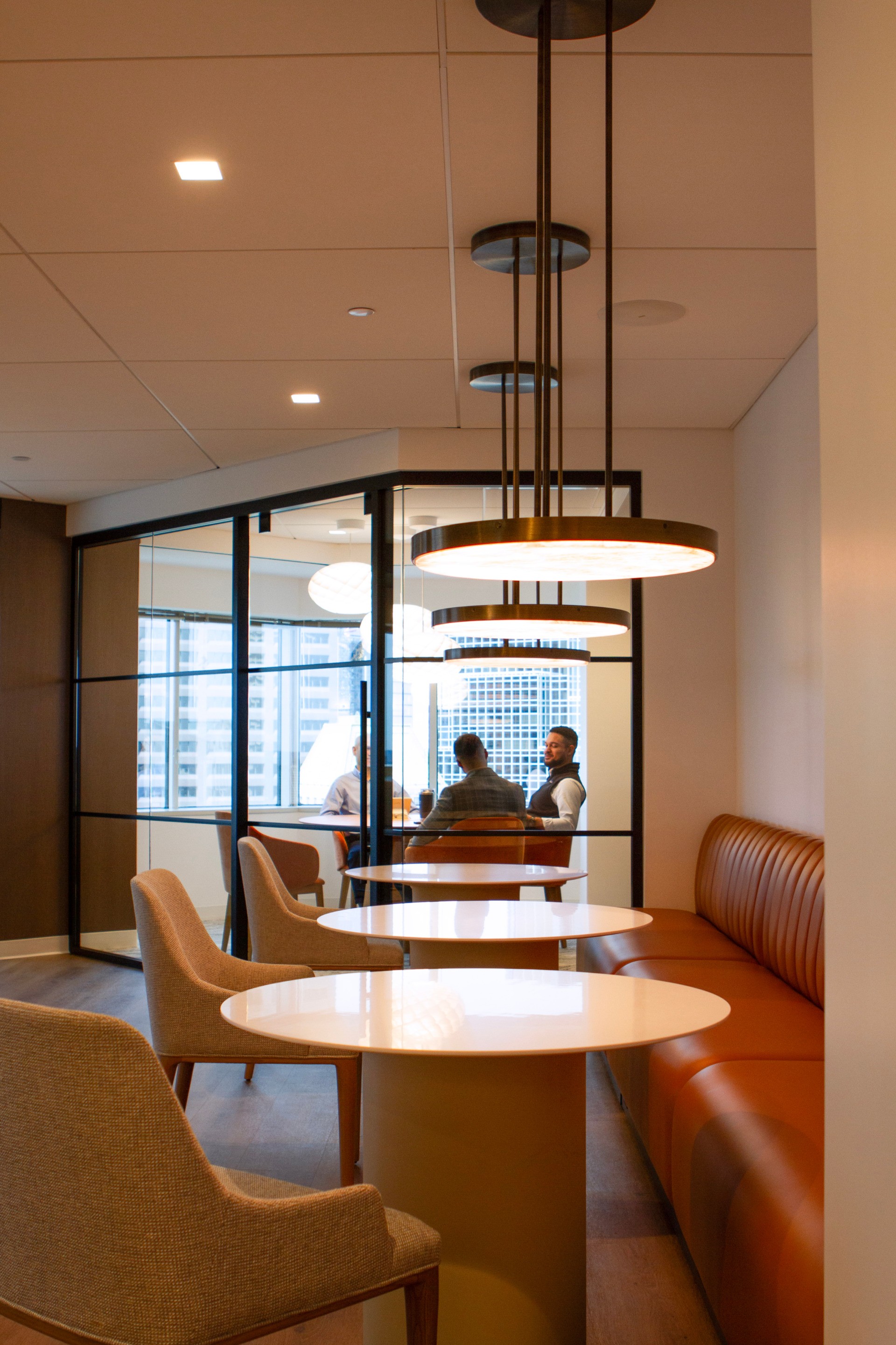 A team built on experience and insight. Employees meeting in Westfield's office longe. Lounge tables in the foreground and the meeting taking place in a glass-wall room in the background.